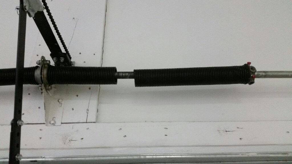 A black broken garage door spring attached to a white garage